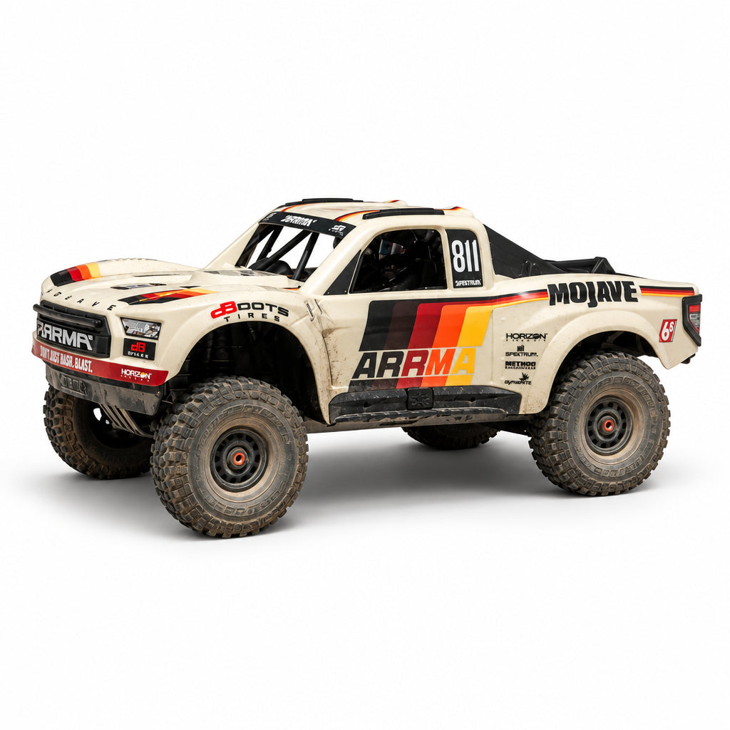 A beige off-road truck with racing decals, including 'MOJAVE' and 'ARMA', driving on a sandy desert track.
