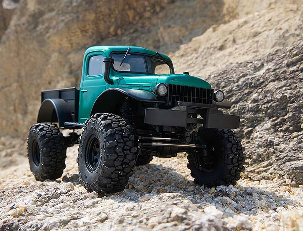 Green FMS Power Wagon RC Crawler on rocky terrain with a mountainous background