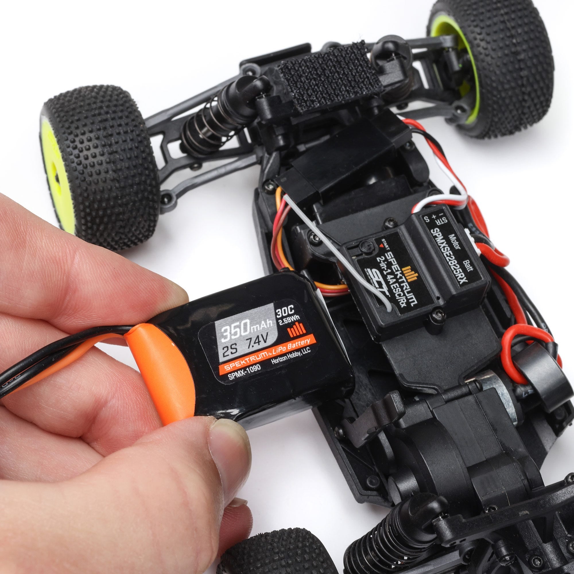 Hand holding a digital battery meter next to a remote control car on a white background