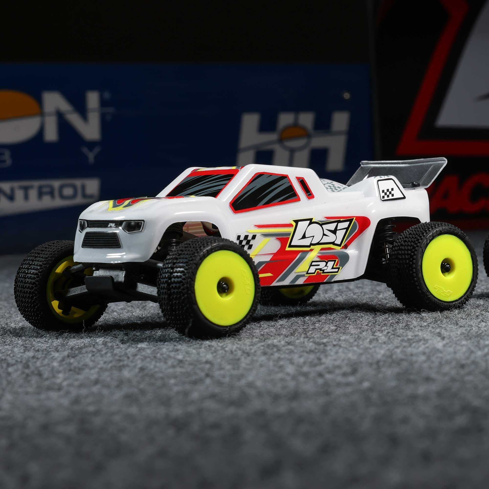 Model truck with yellow wheels on a textured surface, featuring branding in the background.