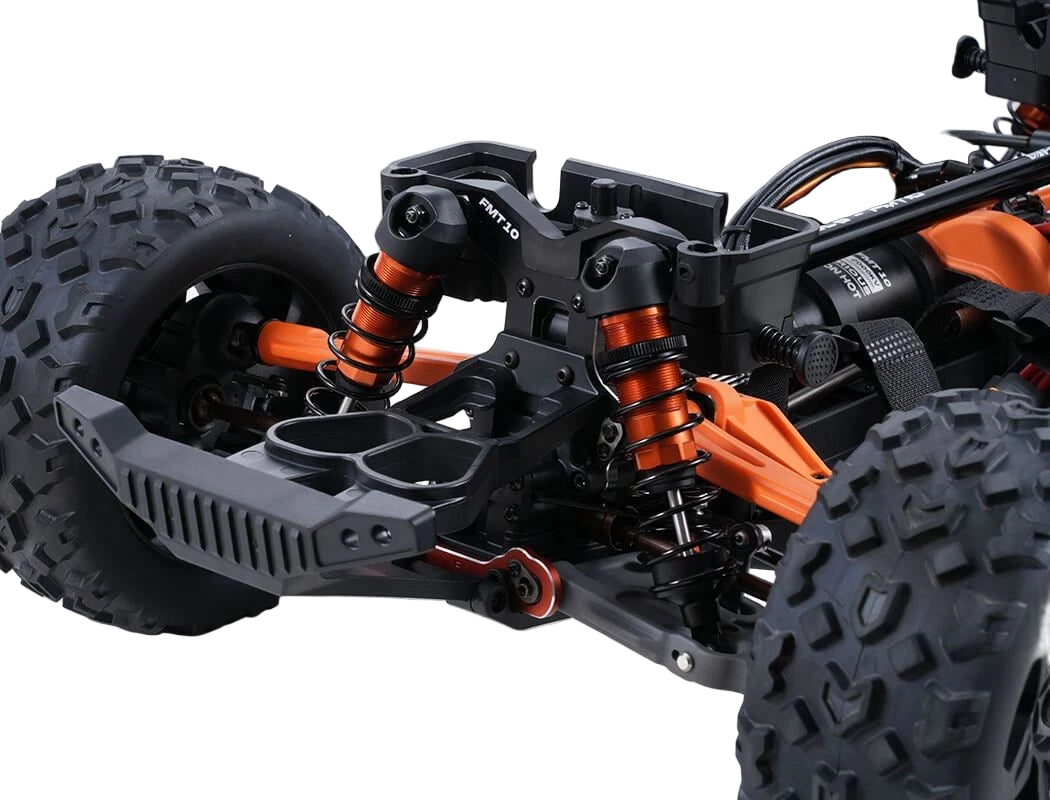 Close-up of a detailed model car chassis with large black tires and orange suspension components on a light gray background.