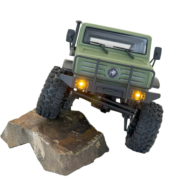 Model of a green off-road vehicle on a rock with glowing headlights.