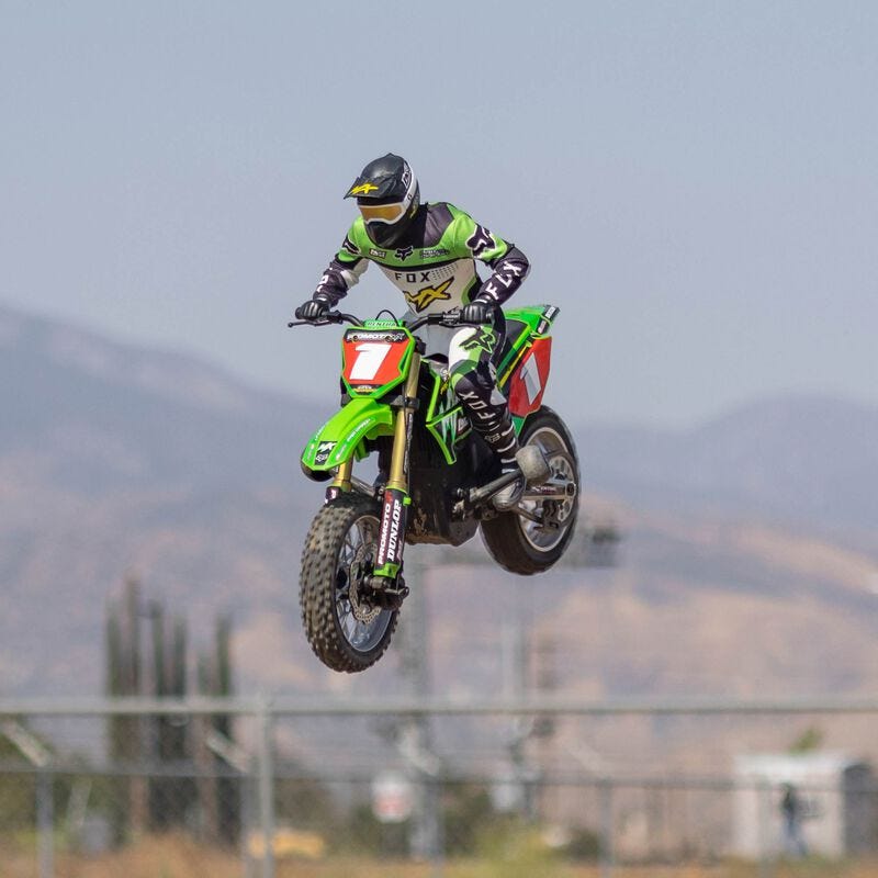  Losi Promoto-MX 1/4 Dirt Bike in mid-air performing a stunt with a green bike on a track.